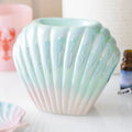Quemador de wax melts con forma de concha nacarada, vista frontal sobre fondo claro, acabado iridiscente elegante