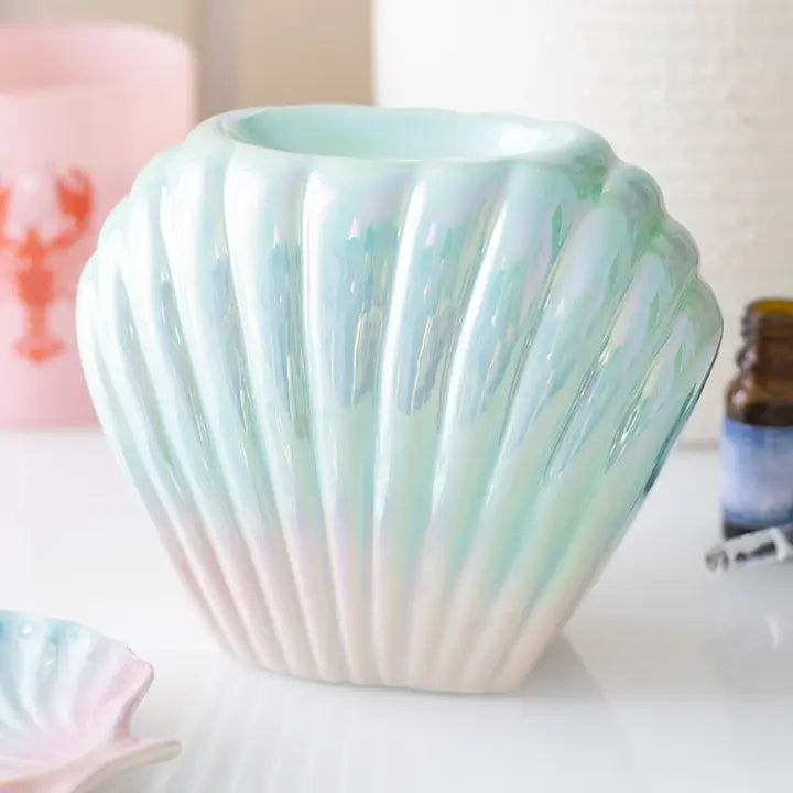 Quemador de wax melts con forma de concha nacarada, vista frontal sobre fondo claro, acabado iridiscente elegante