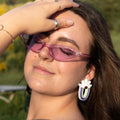 Modelo con pendientes de metacrilato en forma de margarita blanca con centro dorado y arcoíris colgante en tonos pastel.